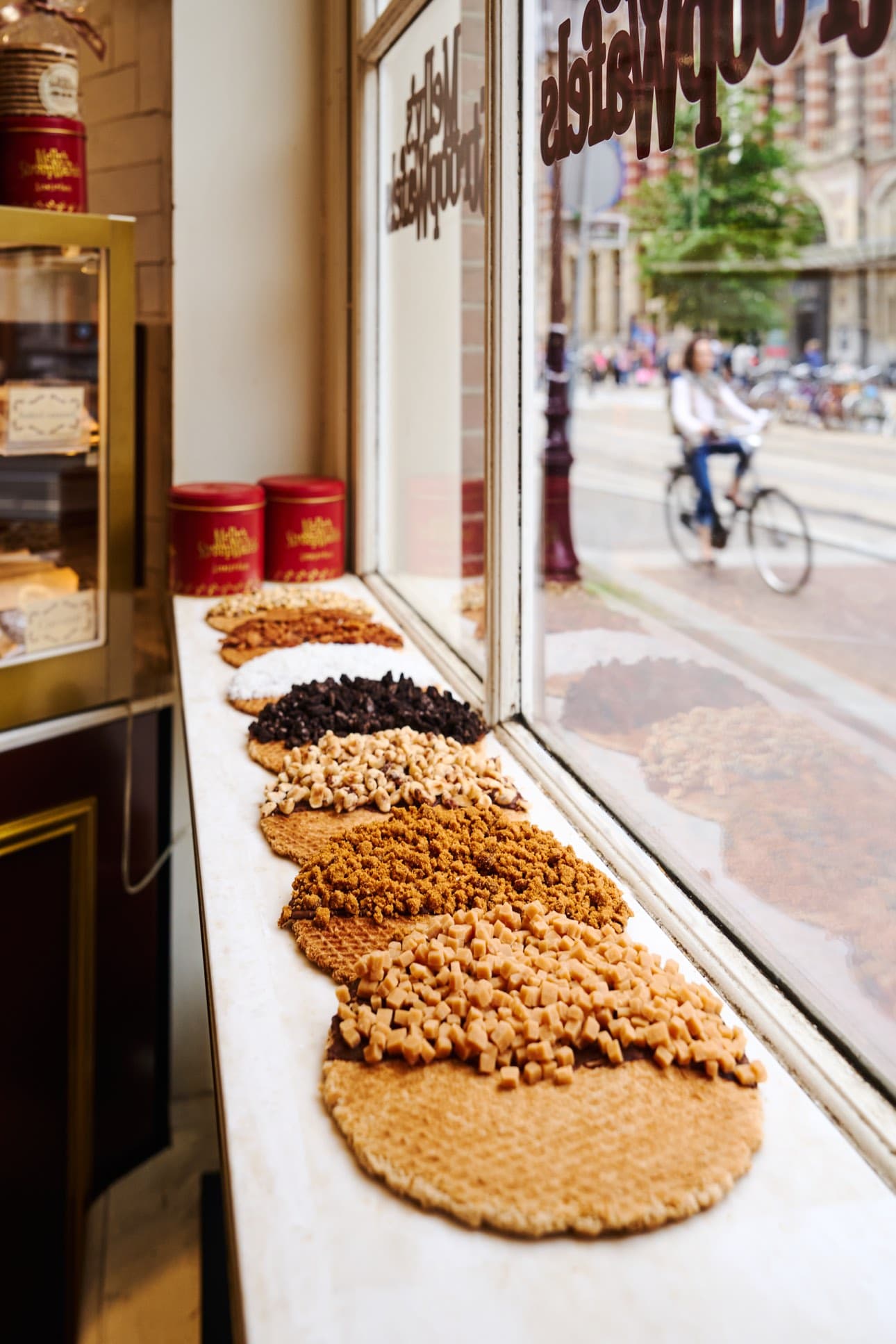 Melly's Stroopwafels shop window in central Amsterdam, with the gold sign and a row of freshly topped stroopwafels and gift tins